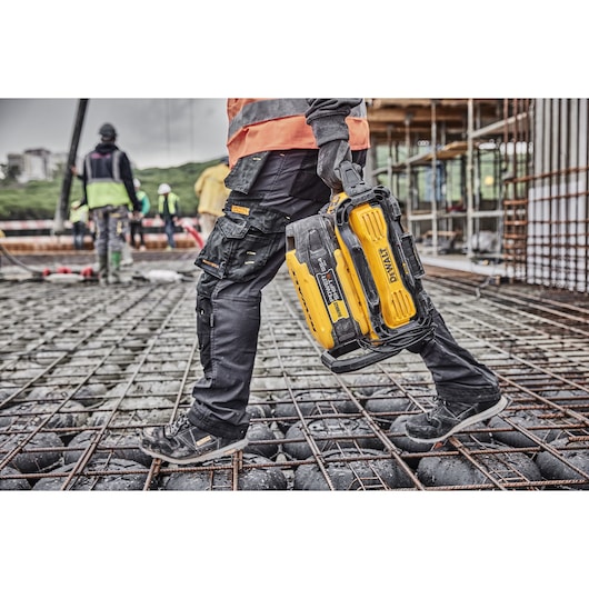 Worker carries Powershift battery DCBPS0554 connected to Powershift 550W Charger DCBPSC0551 across a bed of rebar