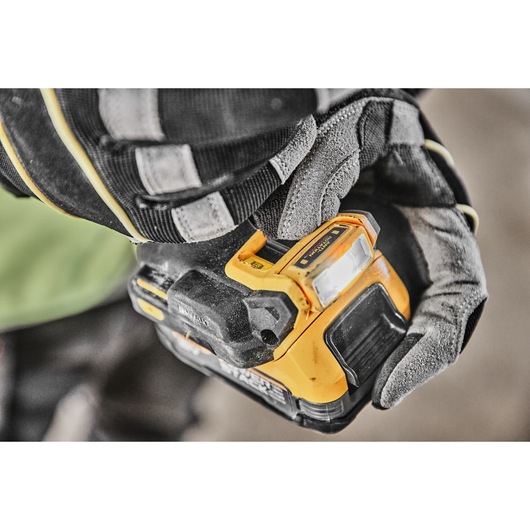 A gloved hand pushing the LED light switch on the base of the DCD800E2T 18V XR Brushless Drill Driver 