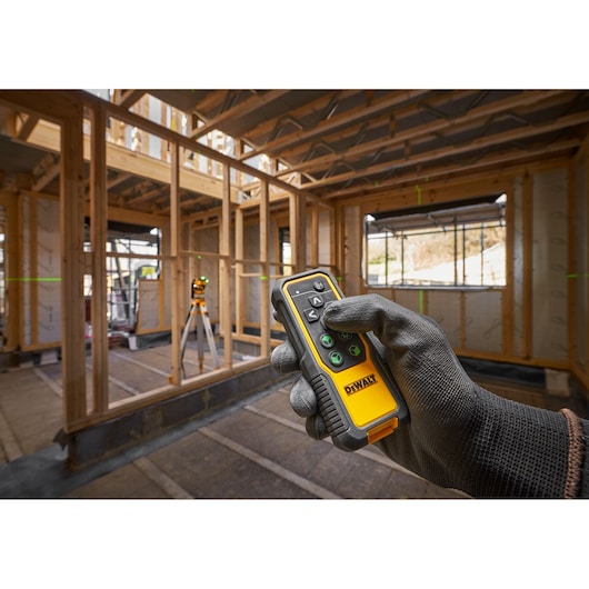 Worker on site holding the 18V 3X 360 Remote Control Laser remote control, adjusting laser line from meters away, laser on tripod in background.