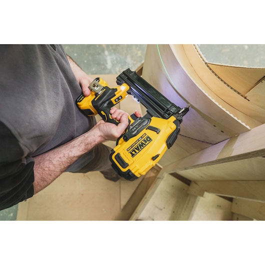 Person using a DEWALT cordless nailer to fasten curved wooden panels on a construction project.