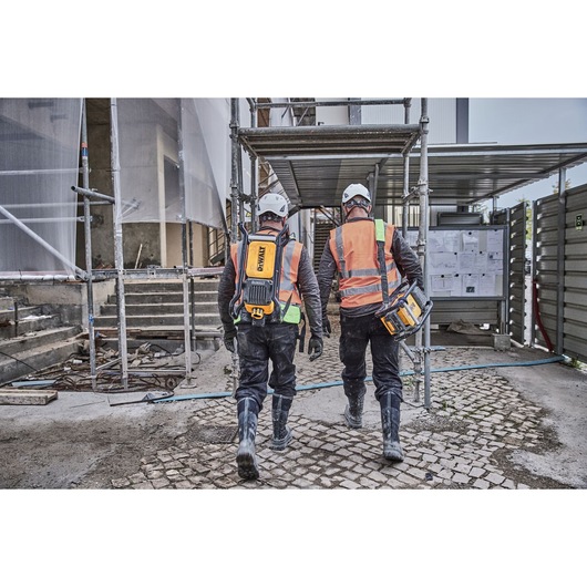 Two construction workers walking off site. Each carries a Powershift Backpack Concrete Vibrator